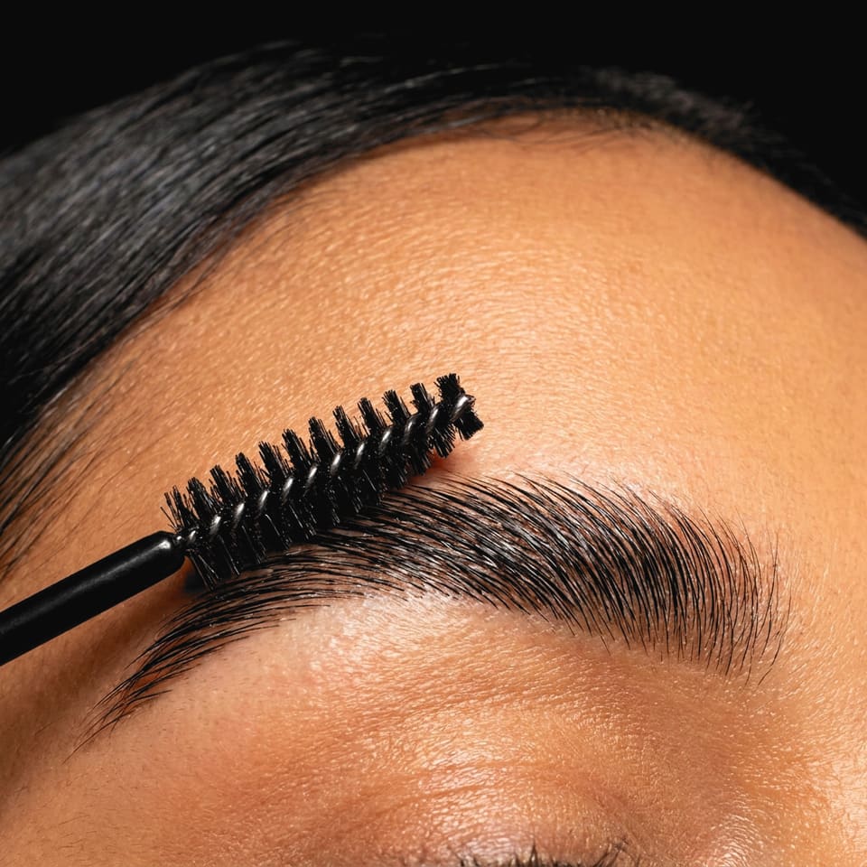 A laminated brow being brushed up with a spoolie, close up