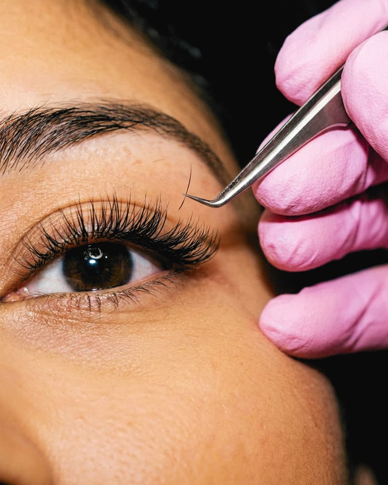Lash extensions going on, close up, a pink gloved hand holding the tweezers