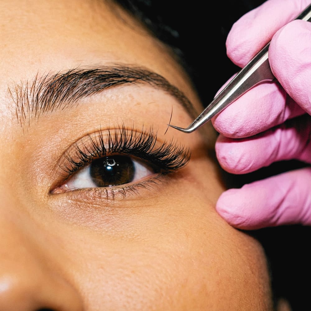 Lash extensions going on, close up, a pink gloved hand holding the tweezers