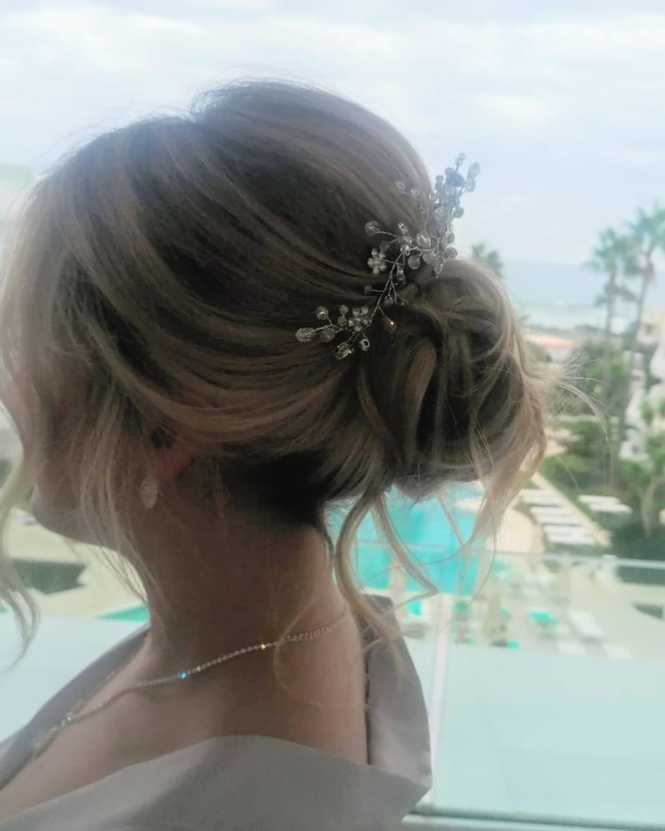 A soft bridal updo with a hair vine, the sea behind