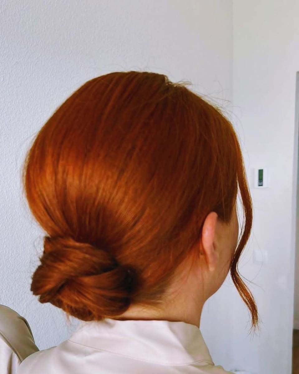 A copper red low bun with face framing strands, from behind